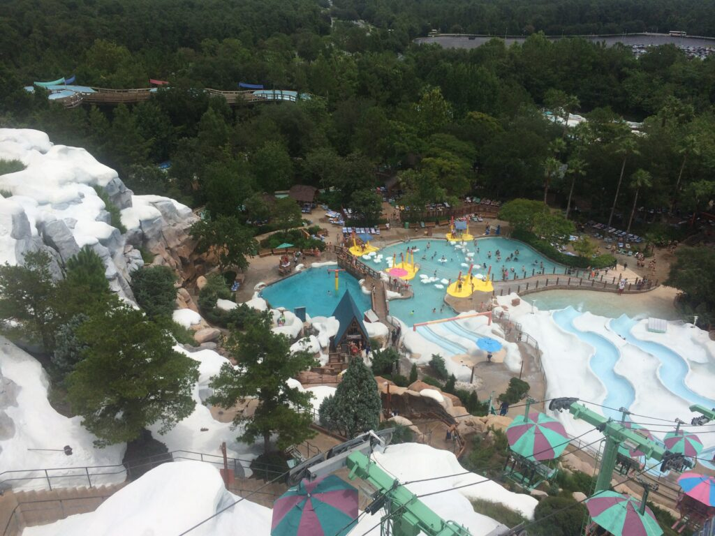 Foto mostra de cima o parque aquático da Disney, Blizzard Beach, suas piscinas e tobogãs que simulam neve derretida. É possível ver o teleférico também.