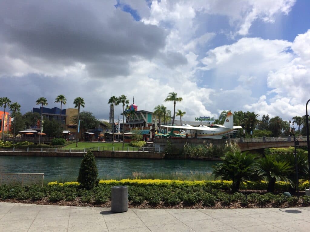 Foto que mostra um panorama do complexo Universal Citiwalk no Universal Orlando Resort. É possível ver um lago e ao fundo temos um modelo de pequeno avião, palmeiras bem altas, lojas e resturantes