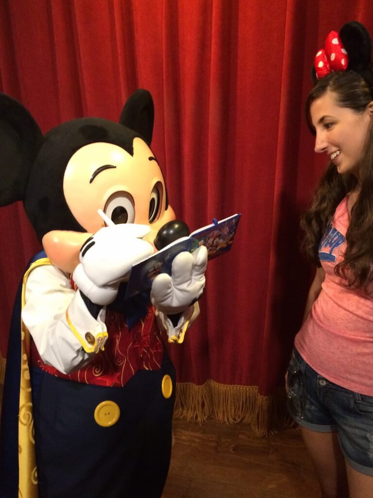 Menina olha o Mickey Mouse, personagem mais clássico da Disney, que assina seu autógrafo em um livrinho da Disney, dentro do parque de diversões Magic Kingdom em Walt Disney World Resort