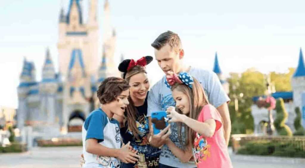 Família composta de uma menina, um menino e um casal de adultos, usa o celular em frente ao castelo da Cinderela no parque Magic Kingdom, em Orlando no Resort Walt Disney World